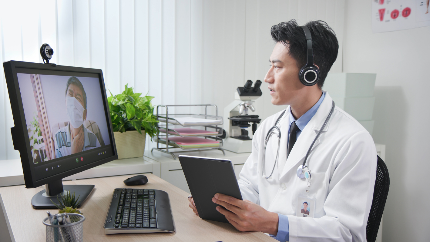 A man in a white lab coat is looking at a computer screen